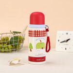 Cute Cartoon Stainless Steel Water BottleCartoon Kids Water BottleCrafty CuddleThermos bottle with red lid and green design on a beige backgroundRed