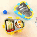 Kids 2 Compartment Lunch Box with Spoon & ForkStainless Steel Lunch BoxCrafty CuddleYellow and blue bento box with compartments filled with food on a light backgroundBlueKidsLunchBox BentoBox LunchBox SchoolLunch KidsEssentials LunchBoxIdeas BackToSchool LeakproofLunchBox KidsLunch TiffinBox