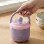 Kids Insulated Soup Lunch Box with HandleStainless Steel Lunch BoxCrafty CuddlePink and purple lunch box with a handle held by a hand on a wooden surface, with 'House of Quirk' branding.PurpleKidsLunchBox InsulatedLunchBox FoodJar SoupContainer KidsEssentials SchoolLunch LunchBoxIdeas HotLunch TiffinBox KidsMeal