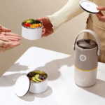 2 Layer Insulated Lunch Box with HandleStainless Steel Lunch BoxCrafty CuddlePerson holding a small container with food next to a larger lunch box on a light surface.GreenLunchBox TiffinBox InsulatedLunchBox LeakproofLunchBox OfficeEssentials KidsLunchBox MealPrepIndia FoodStorage LunchOnTheGo KitchenEssentials