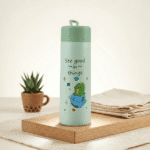 Kids Glass Water BottleCartoon Kids Water BottleCrafty CuddleLight green water bottle with a cartoon design and text on a wooden tray.Green