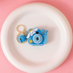 Cute Camera Shape Projector KeychainKeychainsCrafty CuddleBlue camera - shaped keychain with a character design on a white plate against a pink backgroundBlueCuteKeychain KawaiiAccessories KidsAccessories ReturnGiftIdeas CartoonKeychain MiniCamera BagCharm StationeryLove GiftForKids TrendingNow