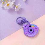 Purple camera-shaped keychain with 'Good Luck' text on a pastel background