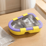 Kids 2 Compartment Lunch Box with Spoon & ForkStainless Steel Lunch BoxCrafty CuddleYellow and purple food container on a wooden surfaceYellowKidsLunchBox BentoBox LunchBox SchoolLunch KidsEssentials LunchBoxIdeas BackToSchool LeakproofLunchBox KidsLunch TiffinBox