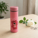 Cartoon Print Glass Water BottleCartoon Kids Water BottleCrafty CuddlePink thermos bottle with a bear design and 'hello' text on a wooden surface with a white rose and green leaves.PinkWaterBottle CuteBottle KidsBottle CartoonBottle GlassBottle SchoolEssentials BackToSchool KawaiiStyle HydrationGoals CuteAccessories