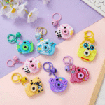Colorful camera-shaped keychains on a pink and purple background with flowers.
