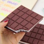 Chocolate bar-shaped notebook held by a hand with red nail polish.