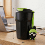 Black tumbler with green lid and character on a desk next to a laptop